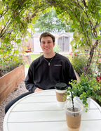 Young man wearing a black Christian Crewneck Sweatshirt sitting at an outdoor table with coffee