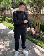 Man wearing a black Christian Crewneck Sweatshirt, styled with matching pants in a garden setting