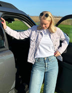 Elevated Faith Christian Jacket in light color worn with a white tee and blue jeans by a car