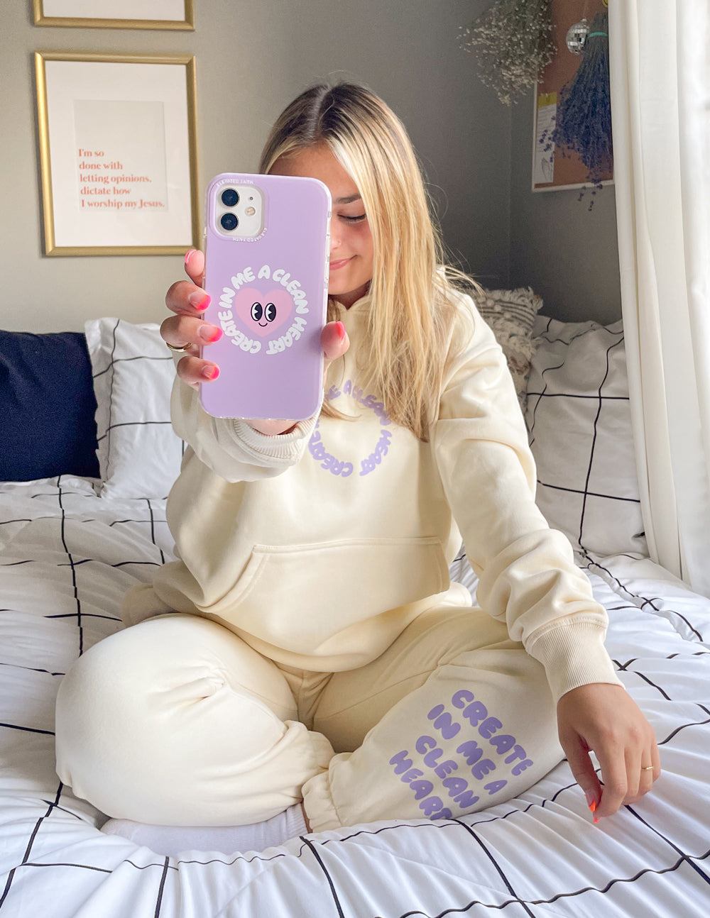 Woman holding a Christian iPhone Case in lavender color while sitting on a cozy bed