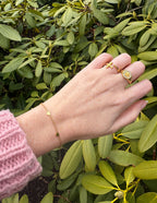 Elevated Faith Christian Jewelry Bracelet featuring delicate hearts on a gold chain worn on a hand among green leaves