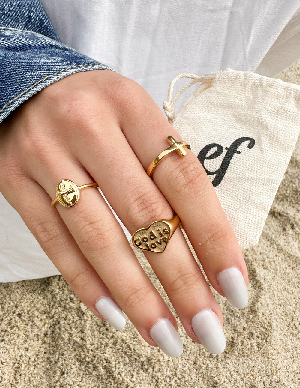 Elevated Faith Christian Jewelry featuring gold rings with heart and cross designs on a woman's hand