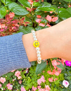 Elevated Faith Christian Jewelry Bracelet with smiley face and pearl beads on a wrist amidst vibrant flowers
