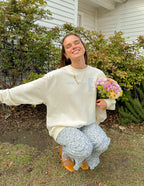 Woman wearing a Christian Crewneck Sweatshirt outdoors, smiling while holding a bouquet of flowers