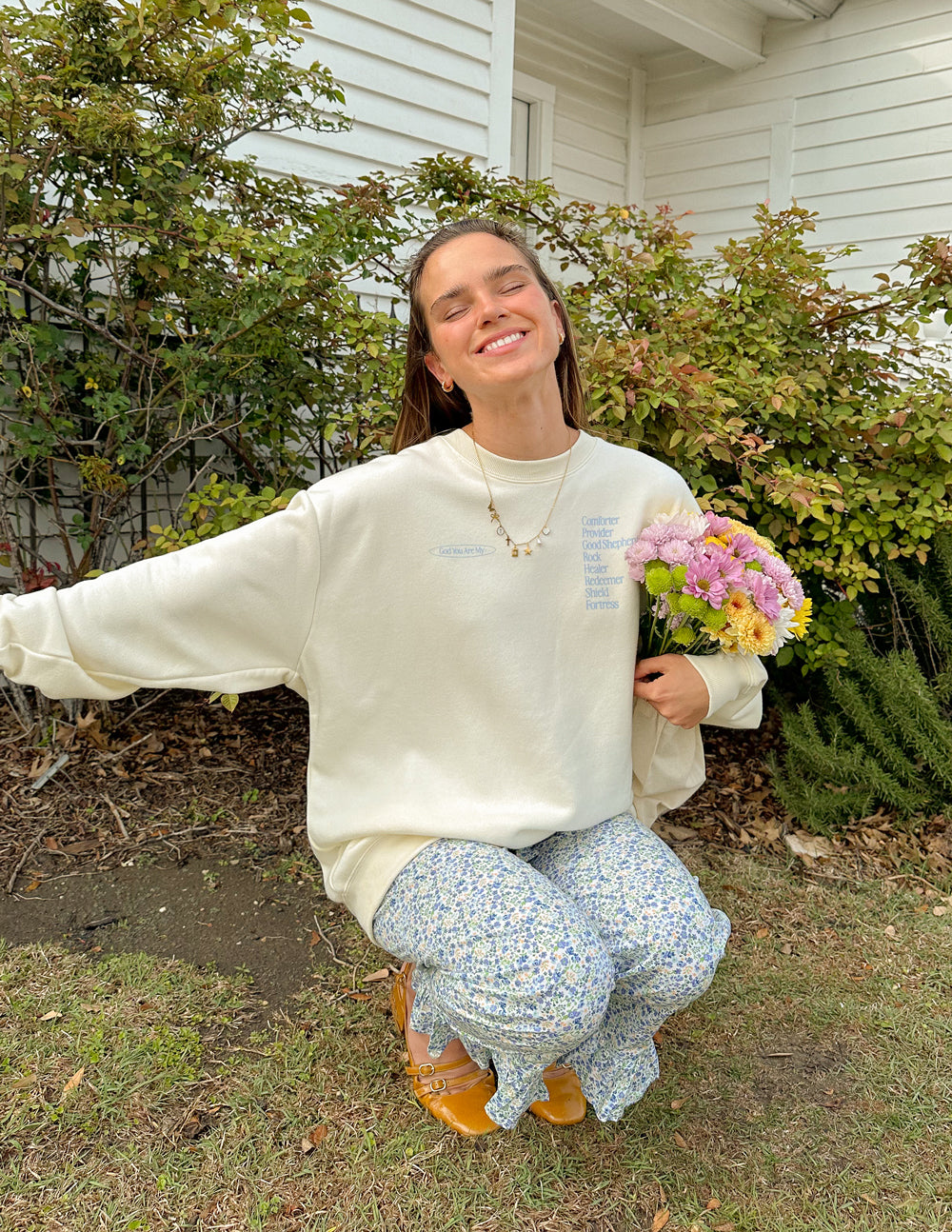 Woman wearing a Christian Crewneck Sweatshirt outdoors, smiling while holding a bouquet of flowers