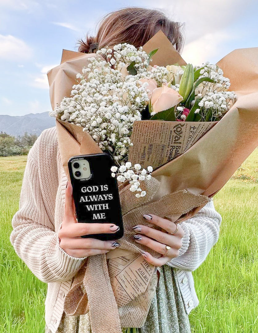 Christian iPhone Case with the phrase God is Always With Me held by a woman with a bouquet of flowers