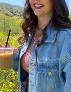 Woman in a denim Christian Jacket from Elevated Faith holding an iced coffee in a flower field