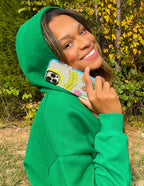 Smiling woman in a green hoodie holding a Christian iPhone Case decorated with floral designs