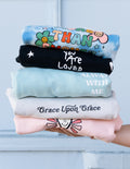 Stack of colorful Christian Crewneck Sweatshirts featuring uplifting messages and designs