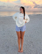 Smiling woman wearing an Elevated Faith Christian Crewneck Sweatshirt on a sandy beach at sunset