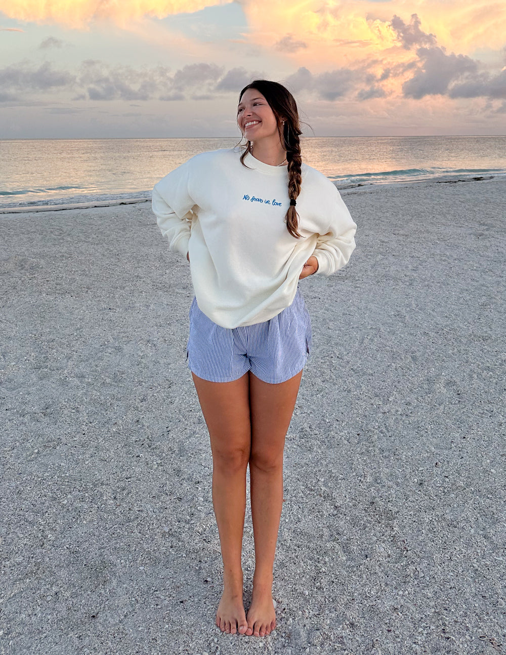 Smiling woman wearing an Elevated Faith Christian Crewneck Sweatshirt on a sandy beach at sunset