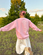 Woman wearing a pink Christian Crewneck Sweatshirt with a floral design on the back standing in a grassy field