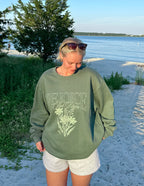 Woman wearing an Elevated Faith Christian Crewneck Sweatshirt with floral design by the beach