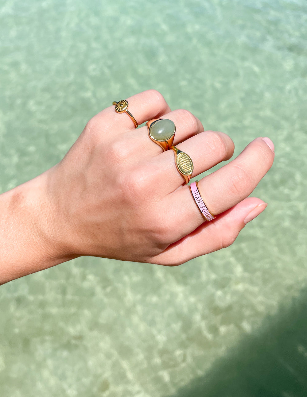 Gold rings on a hand by water, featuring natural stones, perfect for Christian jewelry lovers