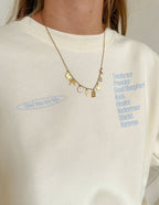 Elevated Faith Christian Jewelry Necklace with Charms and Symbols on a Person Wearing a Cream Sweatshirt