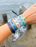 Elevated Faith Christian Jewelry Bracelet collection in various colors worn on wrist by a beach