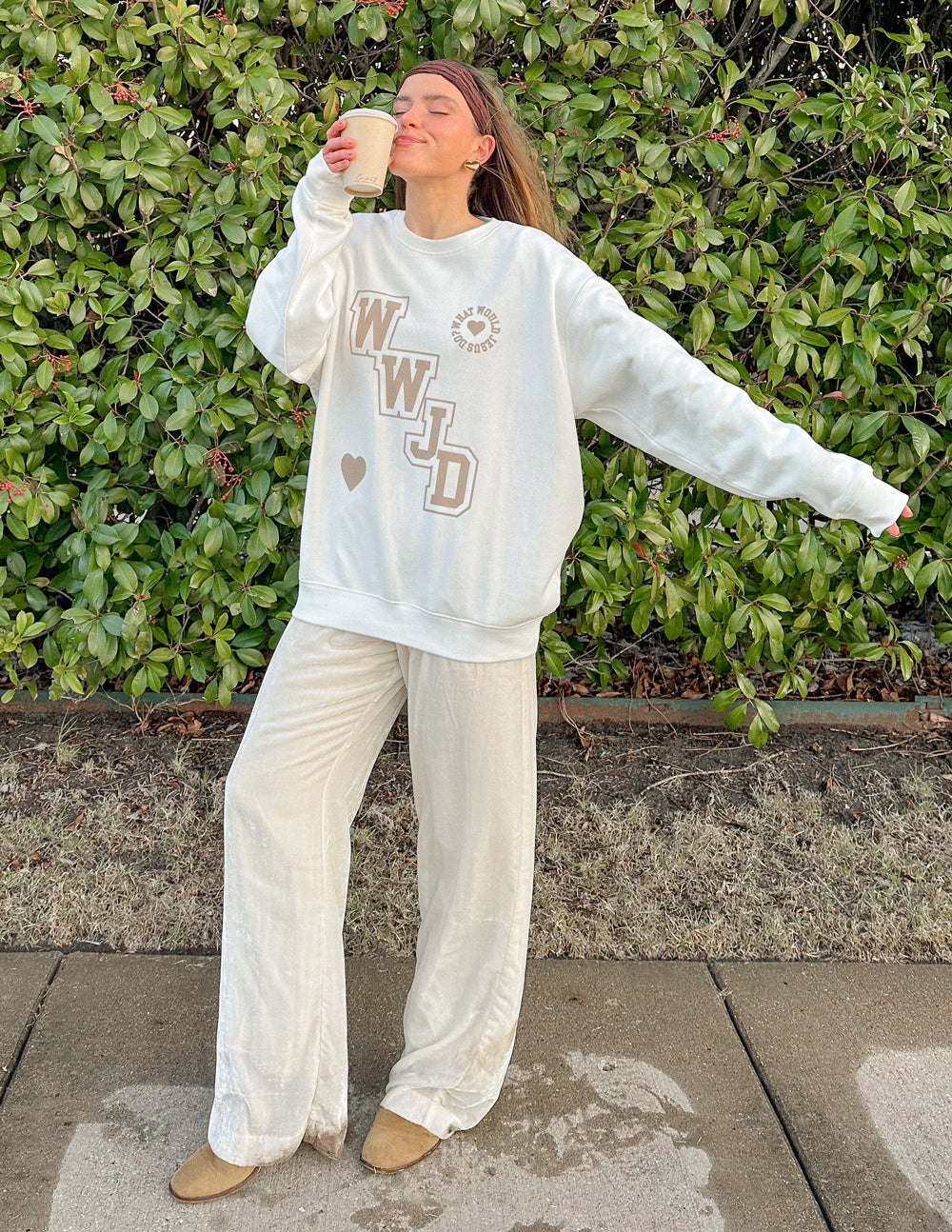 Woman wearing a white Christian Crewneck Sweatshirt with WWJD design, enjoying a coffee outdoors