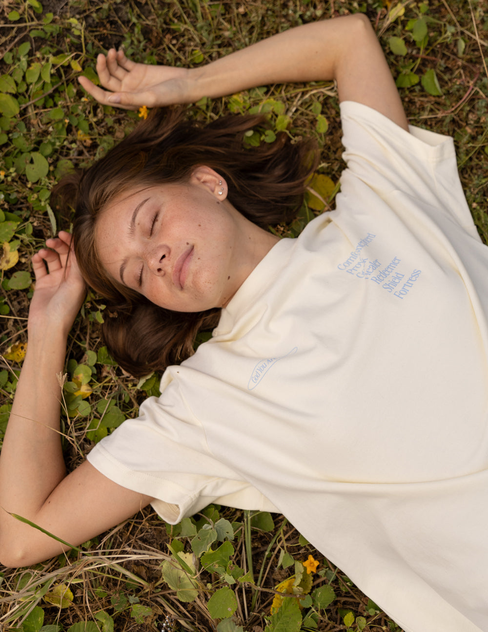 Model lying on the ground wearing a cream Elevated Faith Christian Apparel T-Shirt with inspirational text