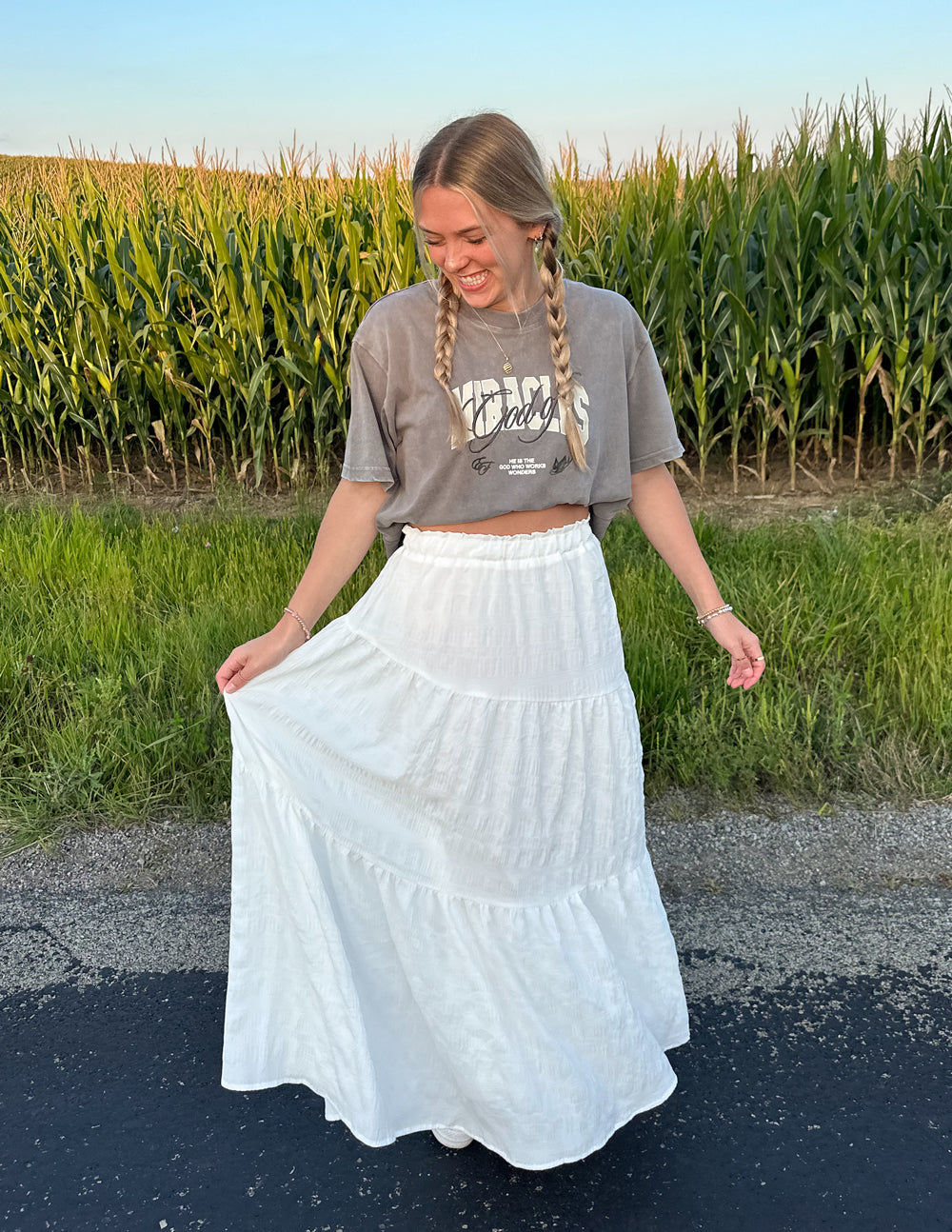 Model wearing Elevated Faith Christian Apparel T-Shirt with a white maxi skirt in a field setting