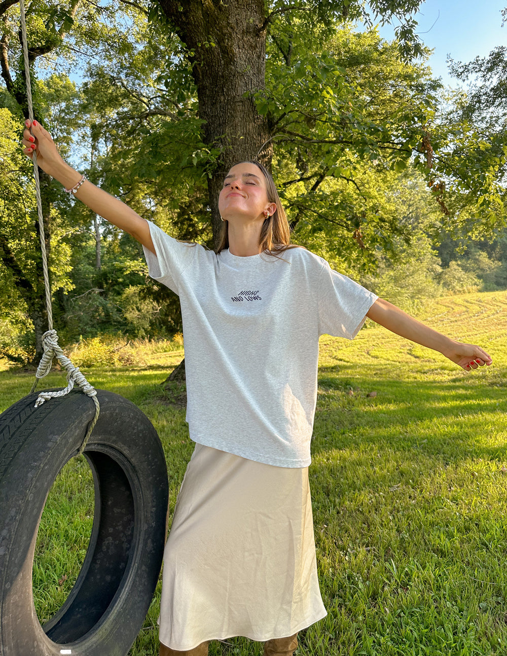 Woman wearing a light gray Christian Apparel T-Shirt, enjoying outdoor scenery with a tire swing