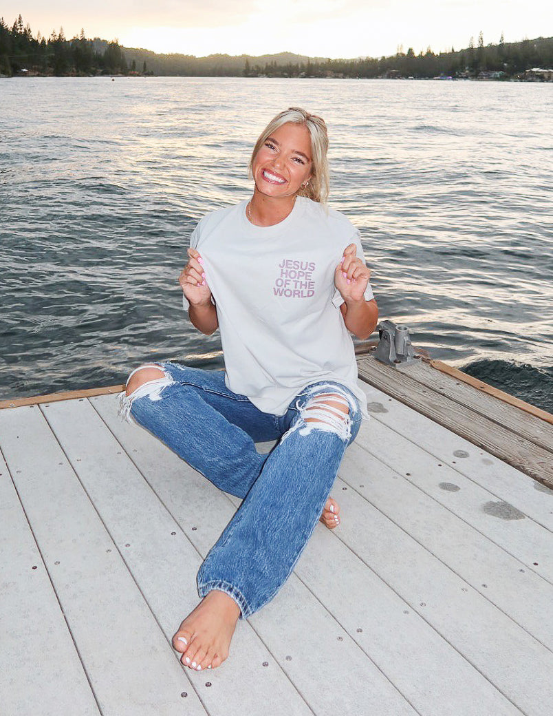 Model wearing Elevated Faith Christian Apparel T-Shirt by the lake at sunset, showcasing a positive message