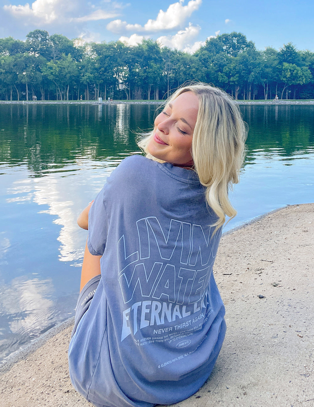 Model wearing Elevated Faith Christian Apparel T-Shirt with Living Water graphic by the lake