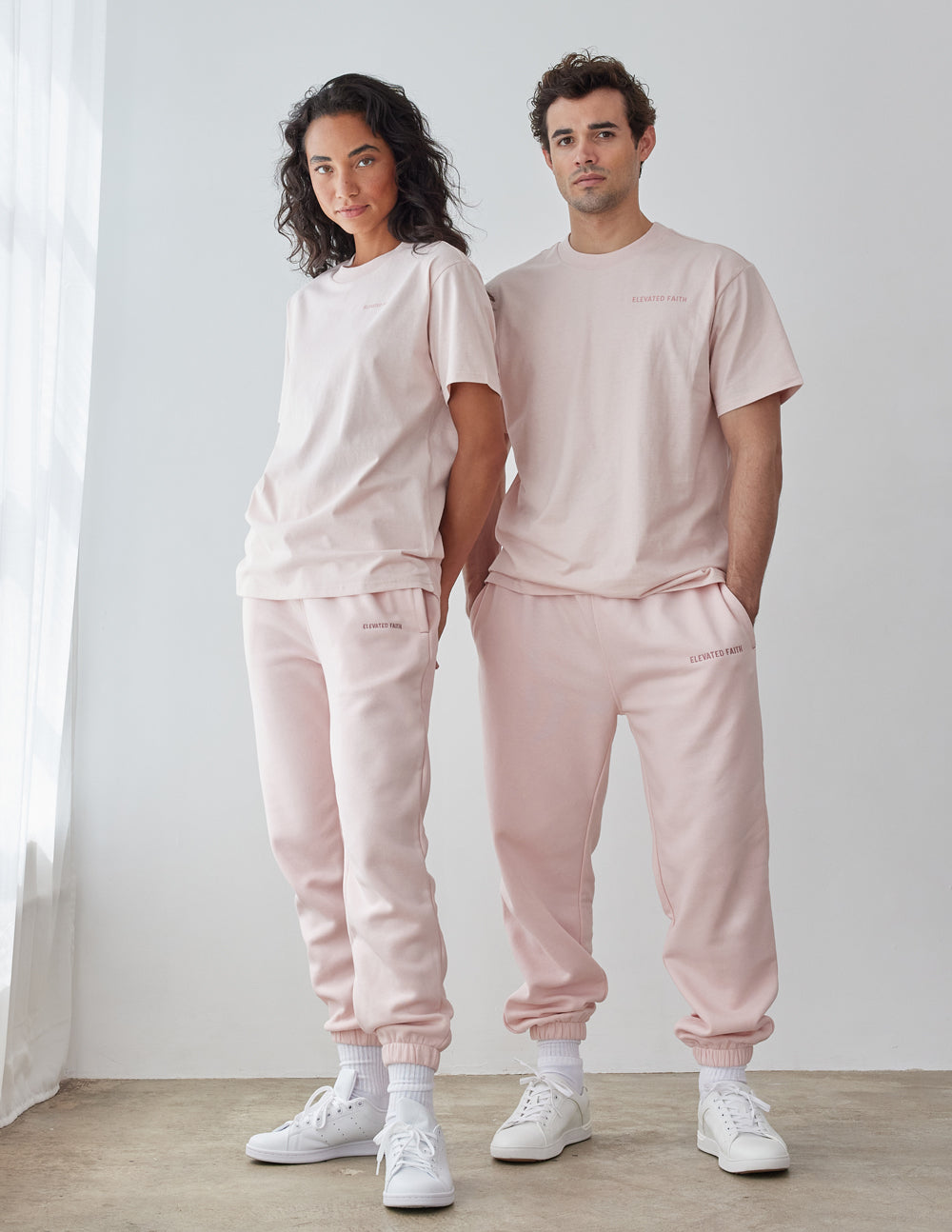 Couple wearing light pink Elevated Faith Christian Apparel T-Shirt with matching sweatpants in a bright space