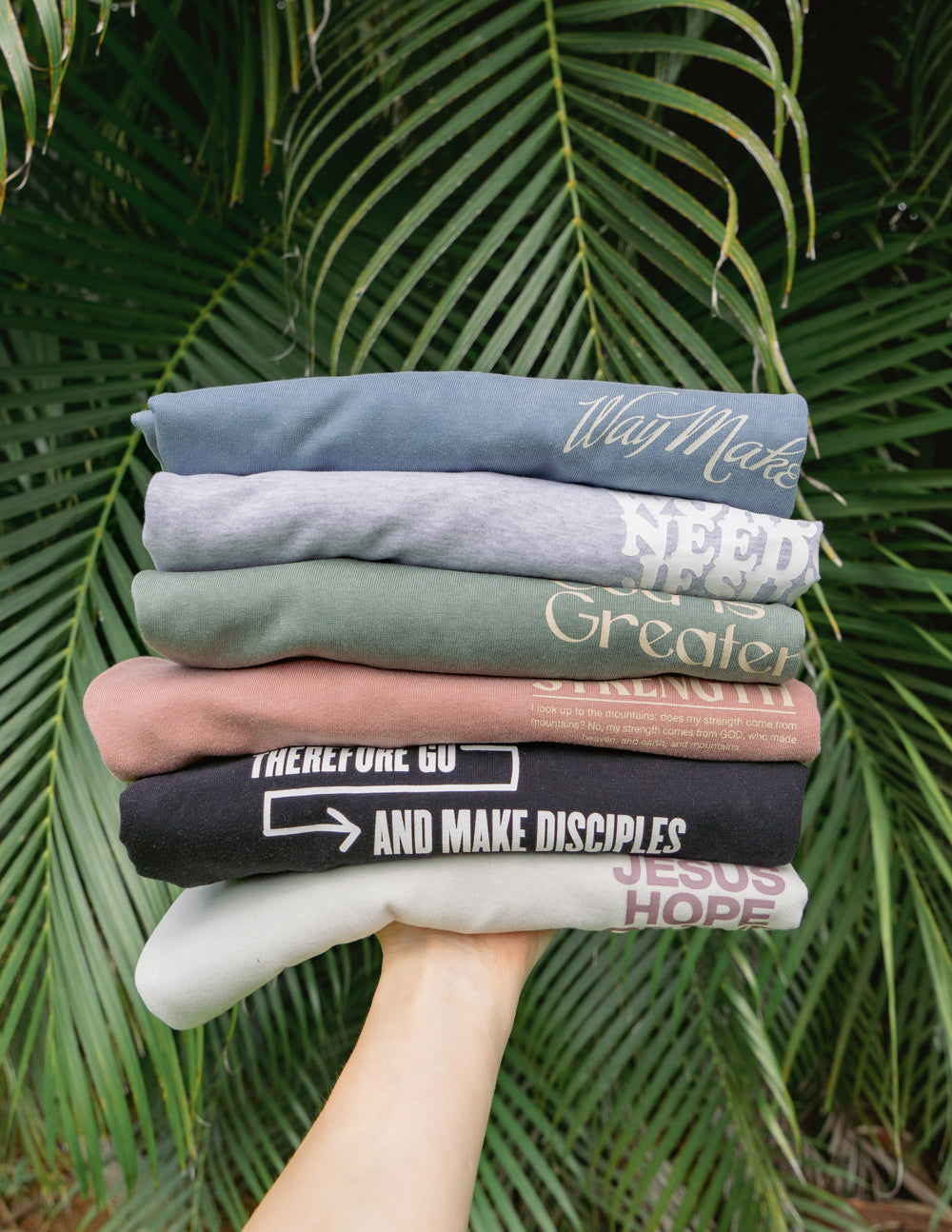 Stack of Elevated Faith Christian Apparel T-Shirts in various colors and messages promoting faith