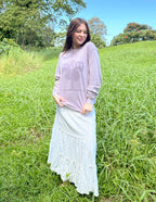 Woman wearing a purple Christian Apparel T-Shirt with floral design outdoors in a green field