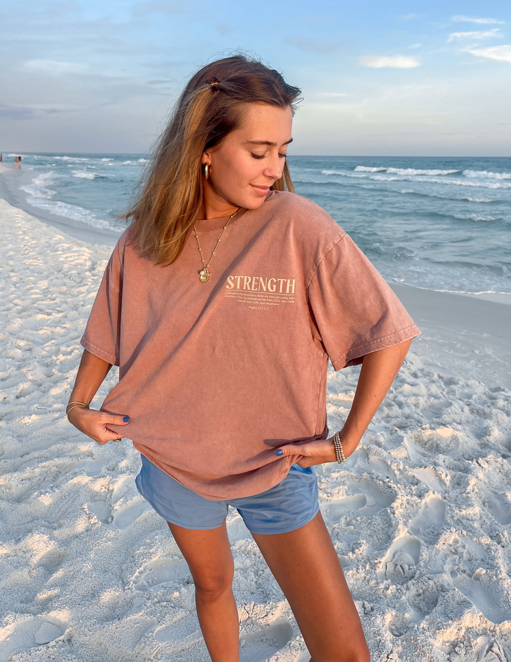 Elevated Faith Christian Apparel T-Shirt in dusty rose color with 'STRENGTH' graphic on a beach setting