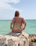 Woman wearing Elevated Faith Christian Apparel T-Shirt on rocks by the sea with a scenic backdrop