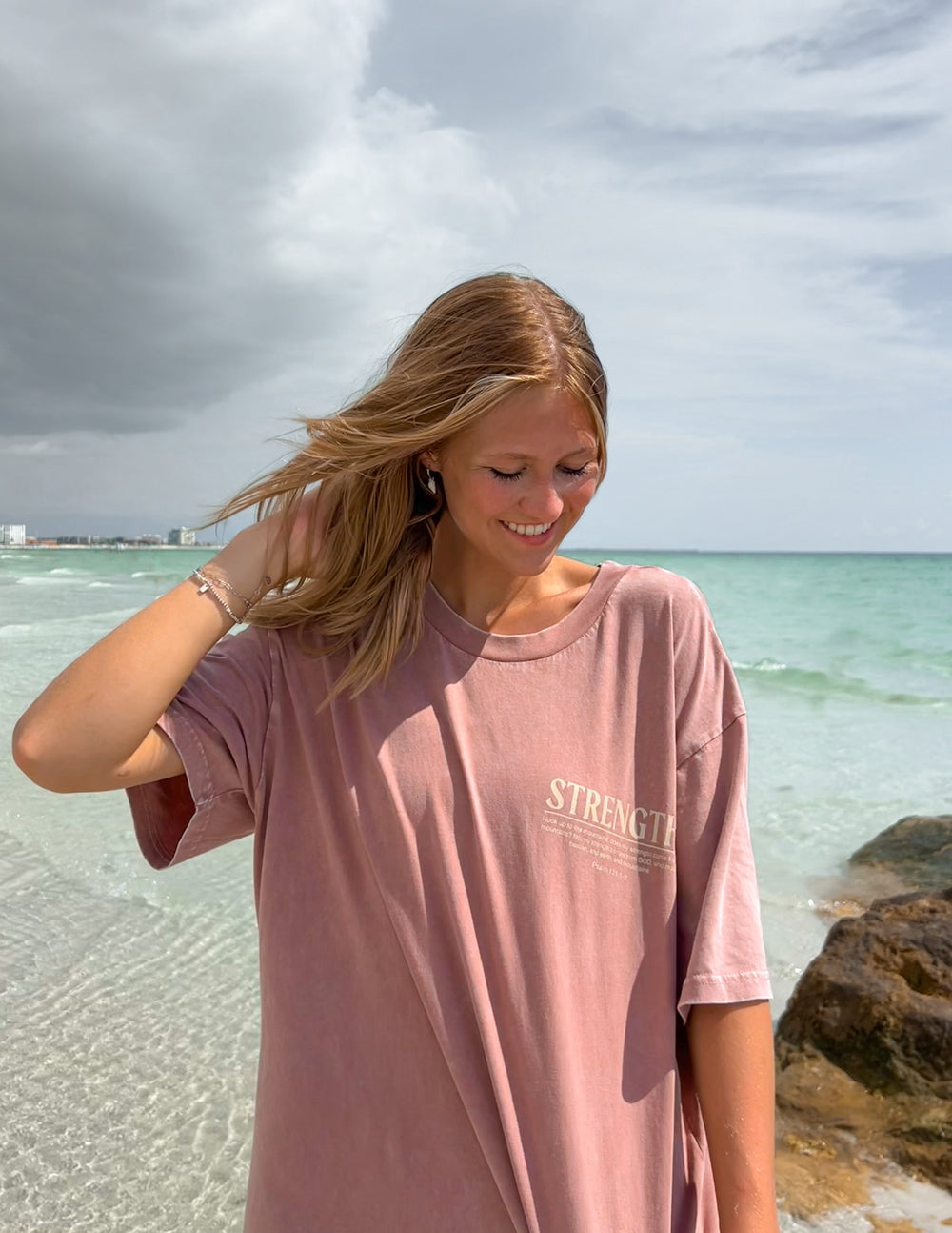 Elevated Faith Christian Apparel T-Shirt in dusty rose with 'STRENGTH' print on the beach