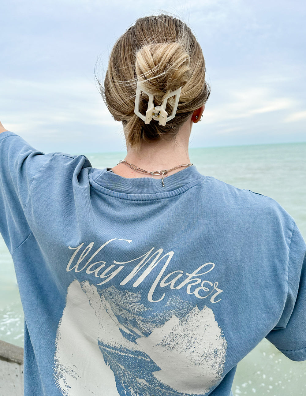 Woman wearing a blue Christian Apparel T-Shirt with a mountain design and 'WayMaker' text back view