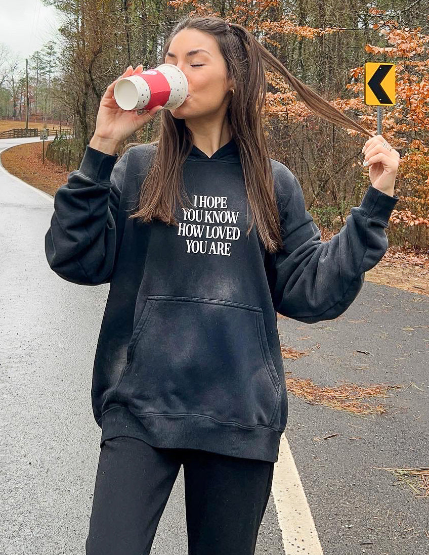Elevated Faith Christian Hoodie in black with inspirational text enjoying a coffee outdoors