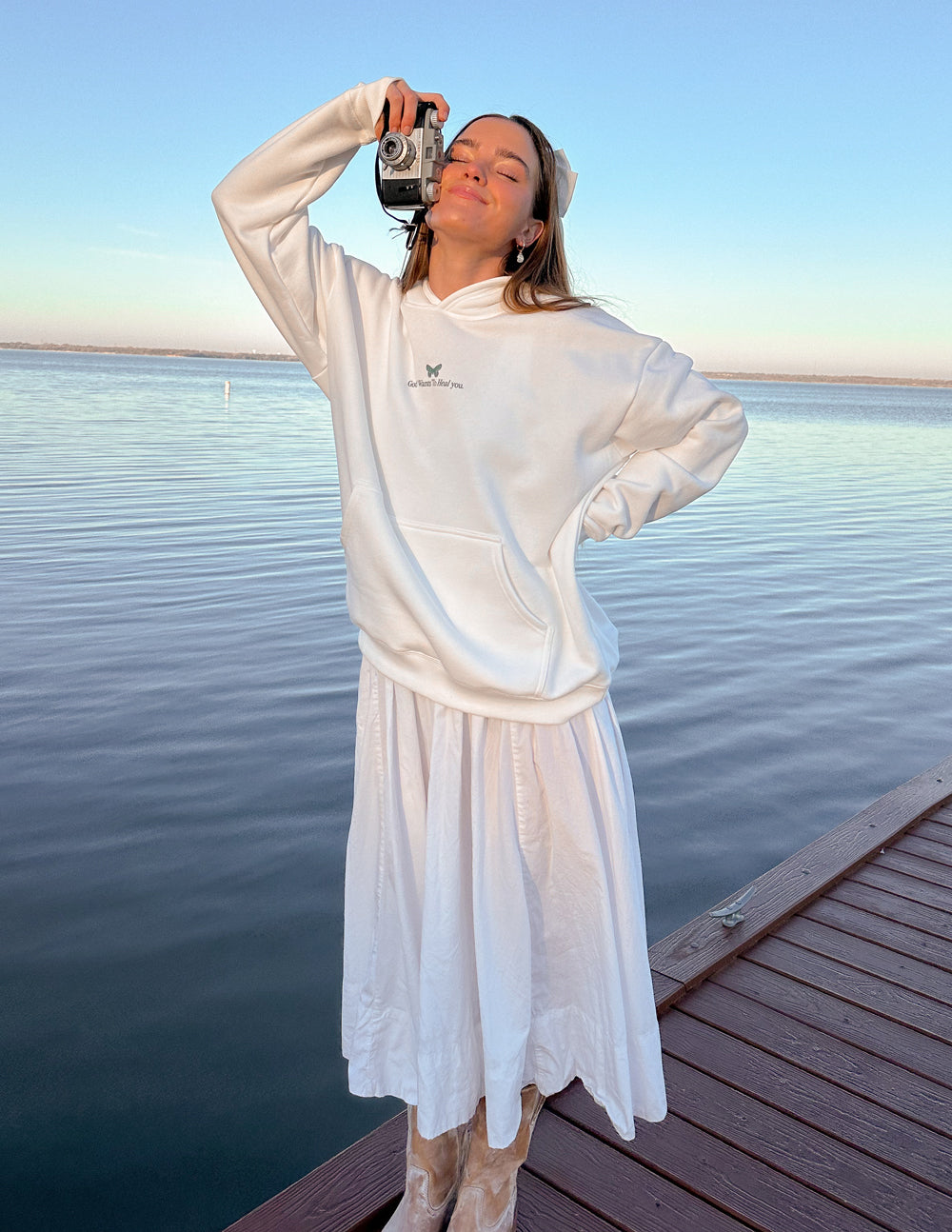 Elevated Faith Christian Hoodie in white, worn by a woman by a lake with a camera