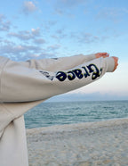 Elevated Faith Christian Hoodie in light gray featuring graphic prints on the sleeves by the beach