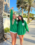Two women wearing green Christian Hoodies posing happily on a sunny palm tree-lined street