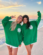 Two women wearing green Christian Hoodies with a beach sunset background, promoting faith and friendship