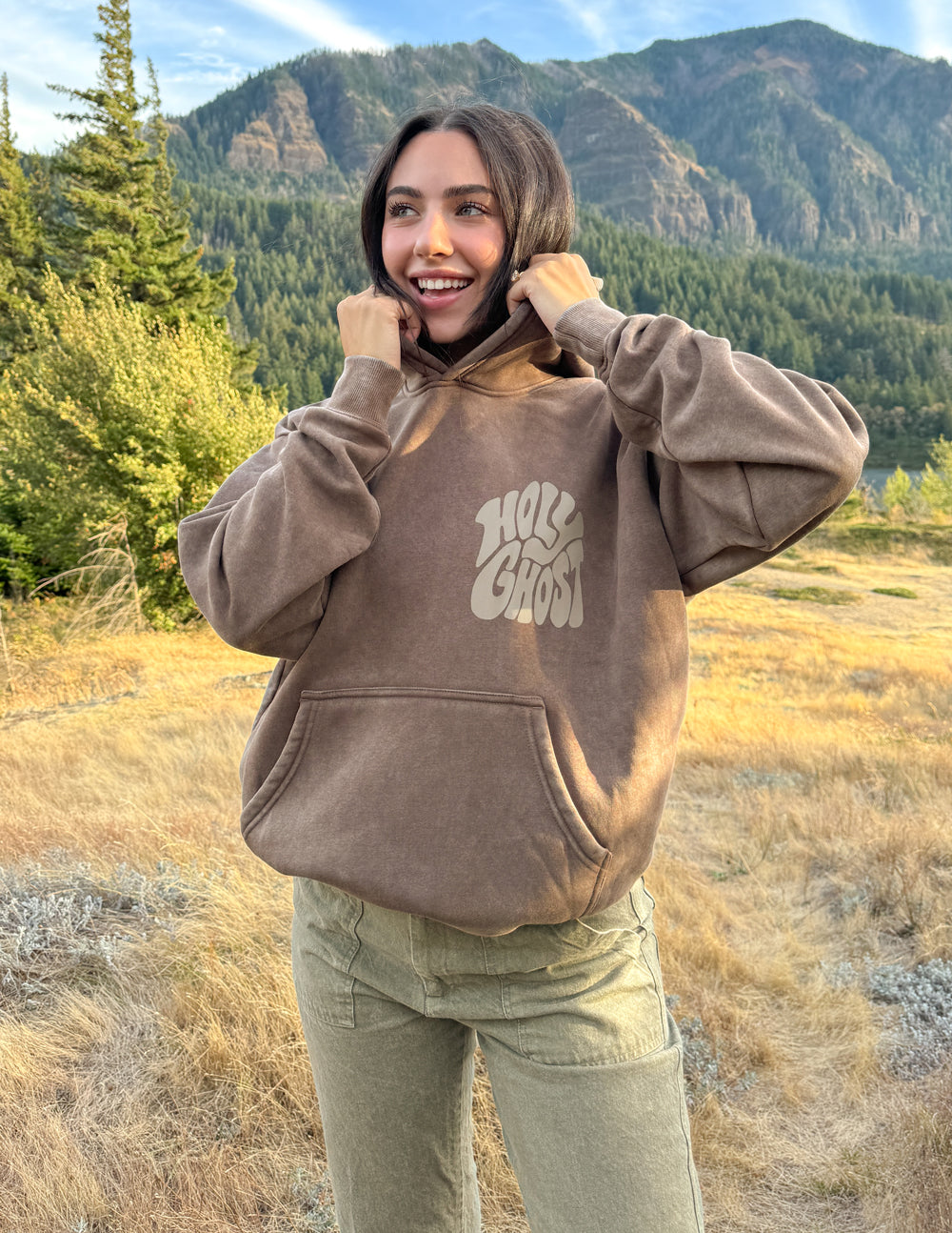 Elevated Faith Christian Hoodie in brown with 'Holy Ghost' graphic on a woman outdoors