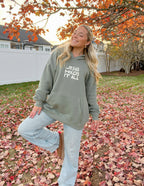 Elevated Faith Christian Hoodie in olive green with 'Jesus Holds It All' text design outdoors in autumn leaves