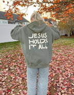 Elevated Faith Christian Hoodie featuring the text Jesus Holds It All on the back in a stylish design