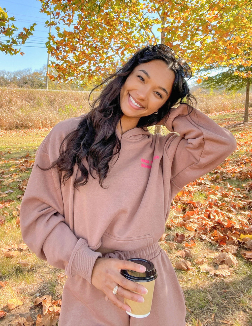 Woman wearing a stylish Christian Hoodie in brown, smiling while holding a coffee cup outdoors