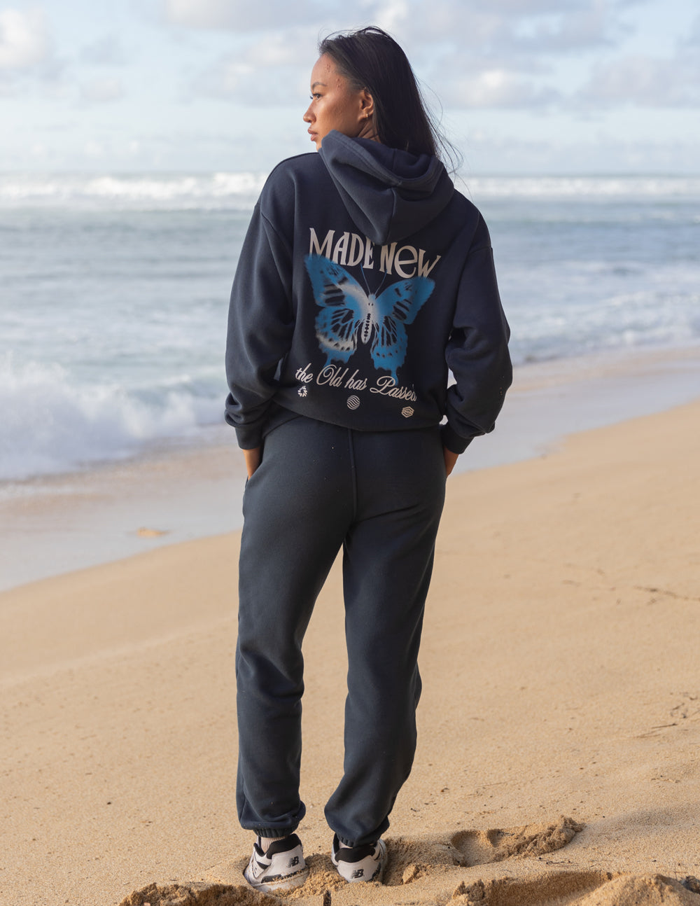 Model wearing a dark blue Christian Hoodie with butterfly design on the back while standing on the beach