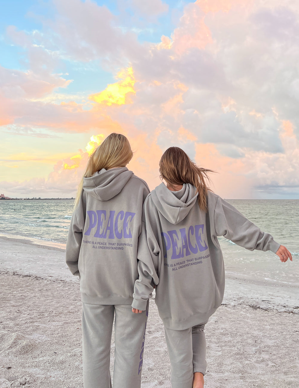 Two women on the beach wearing Elevated Faith Christian Hoodie with 'Peace' graphic design