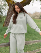 Woman wearing a soft green Christian Hoodie from Elevated Faith, styled with matching pants