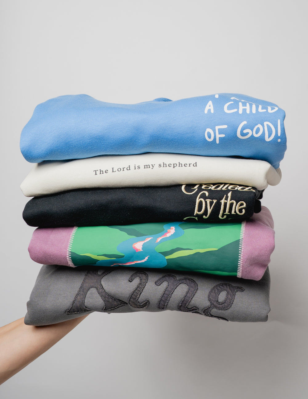 Stack of Elevated Faith Christian Hoodies in various colors with inspiring messages and designs