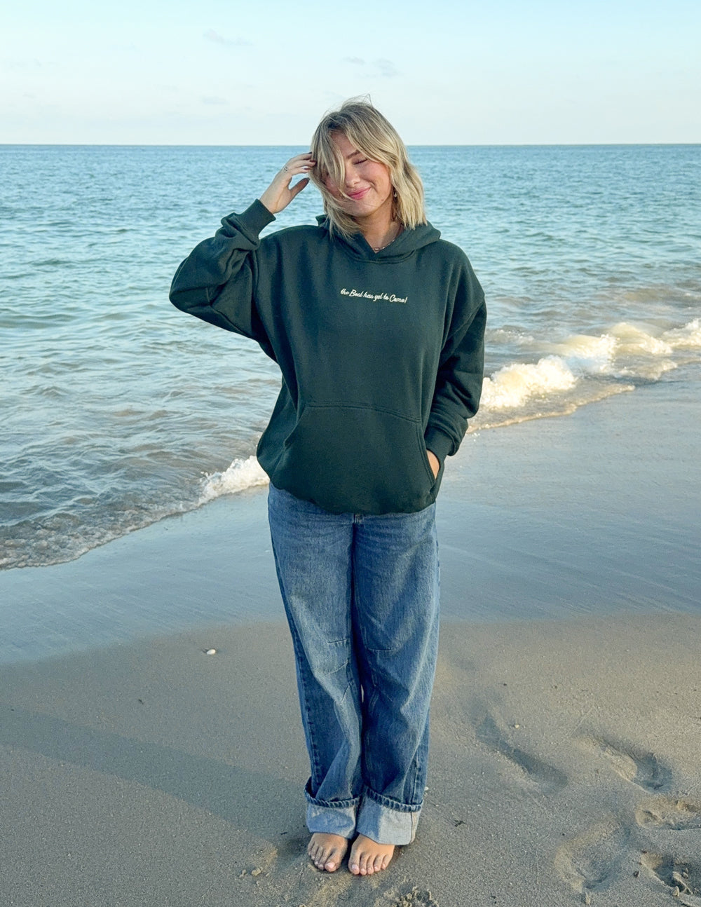 Elevated Faith Christian Hoodie in dark green, featured on a beach with a calm sea backdrop