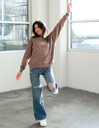 Woman in a brown Christian Hoodie from Elevated Faith dancing in a modern, bright space
