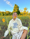 Elevated Faith Christian Hoodie in cream with 'Your Love Never Fails' design among wildflowers