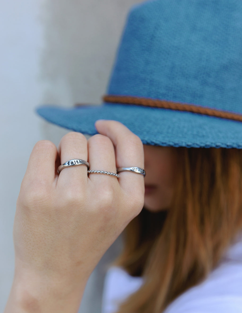 Elevated Faith Christian Jewelry rings displayed on a hand with a blue hat in the background
